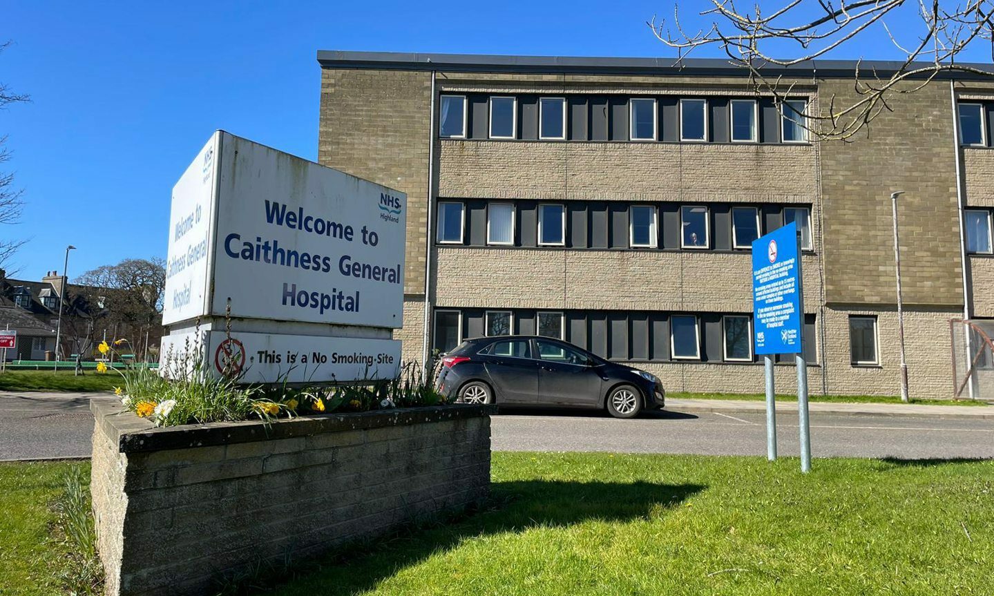 Exterior view of main sign and building of Caithness General Hospital with a black car parked outside. 