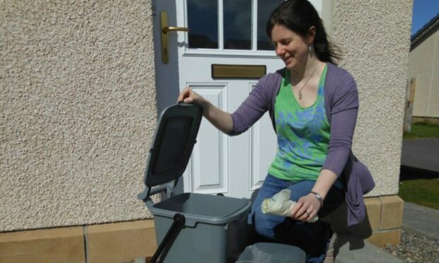 A woman in a green top looks at a grey bin for Highland Council's kerbside food recycling scheme.