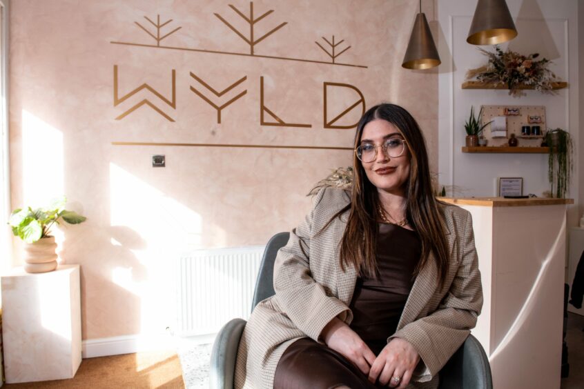 Marcia sits in front of the Wyld Beauty Aberdeen design on her salon wall.