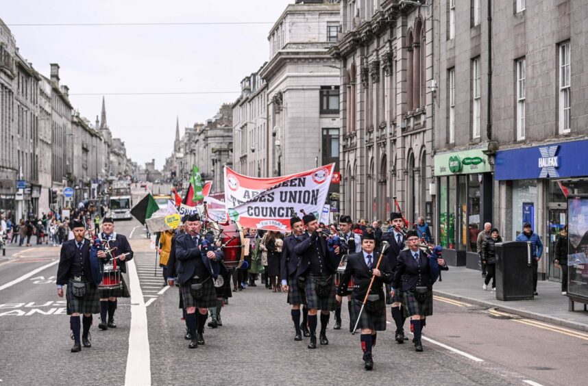 A pipe band leads workers along Aberdeen's Union Street during march.