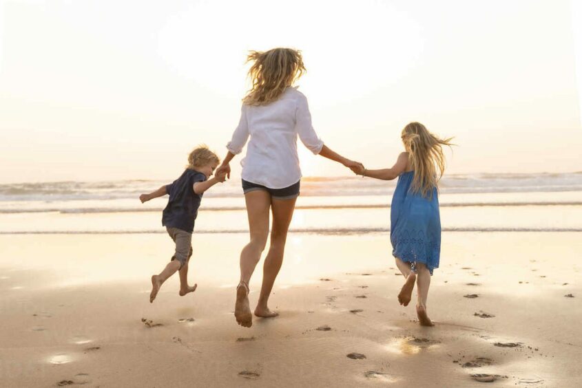 Mum and two kids running on a sunny beach.