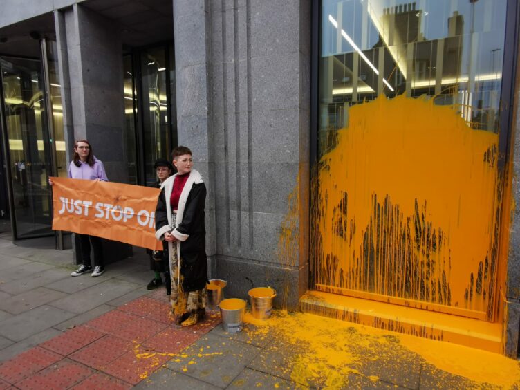 Three protestors hold a 'Just Stop Oil' sign while standing next to the Silver Fin building in Aberdeen which they've splashed with orange paint.