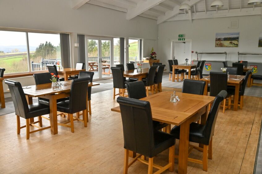 The interior of the club house, featuring wooden dining tables and black leather chairs
