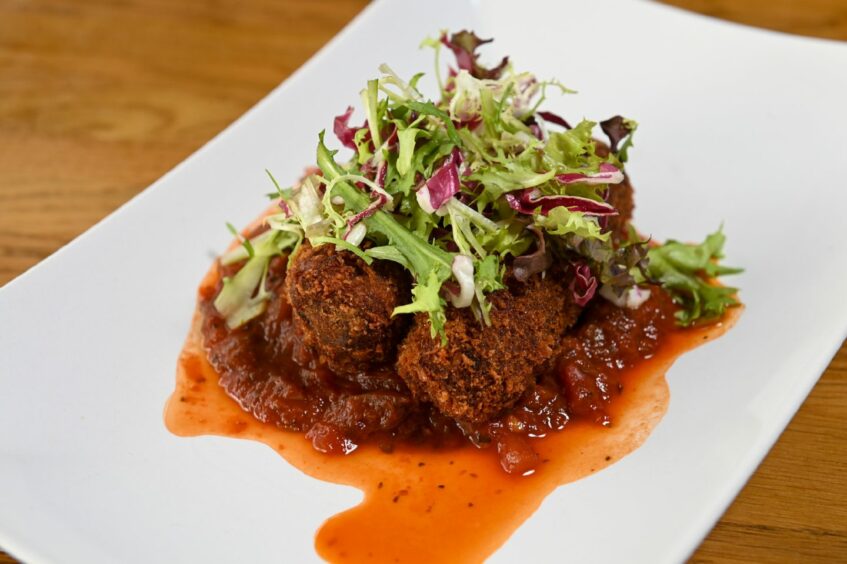 Pork croquettes in a red sauce topped with salad