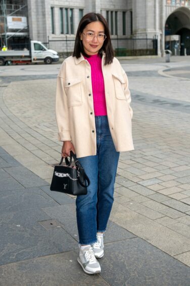 Woman wearing a pink knit top, blue straight-leg jeans, trainers and an oversized white button up.