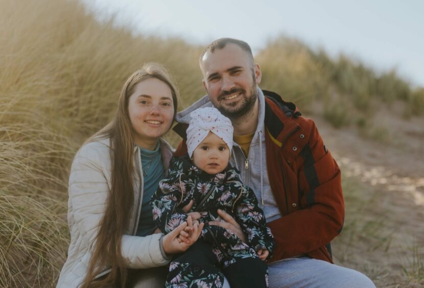 With sand dunes behind them, Yuliia, Artur and their baby are pictured smiling, nestled closely together on Balmedie beach.