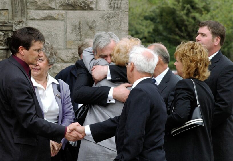 Arlene Fraser's loved ones hug each other at a memorial service in Elgin