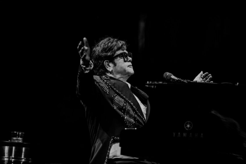 Elton John addressing the audience in black and white at his Liverpool show in 2023.