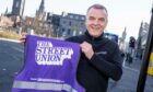 Bob Christie standing holding a purple hi-vis vest with the Our Union Street logo.