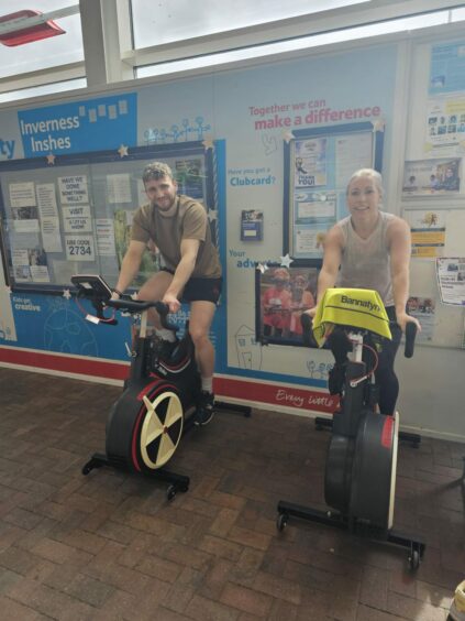 Jackson and Suzanne sitting on spin bikes in the Tesco Inshes store 