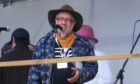 Robe Ellen in a plaid shirt and with a cowboy hat on standing at a microphone.