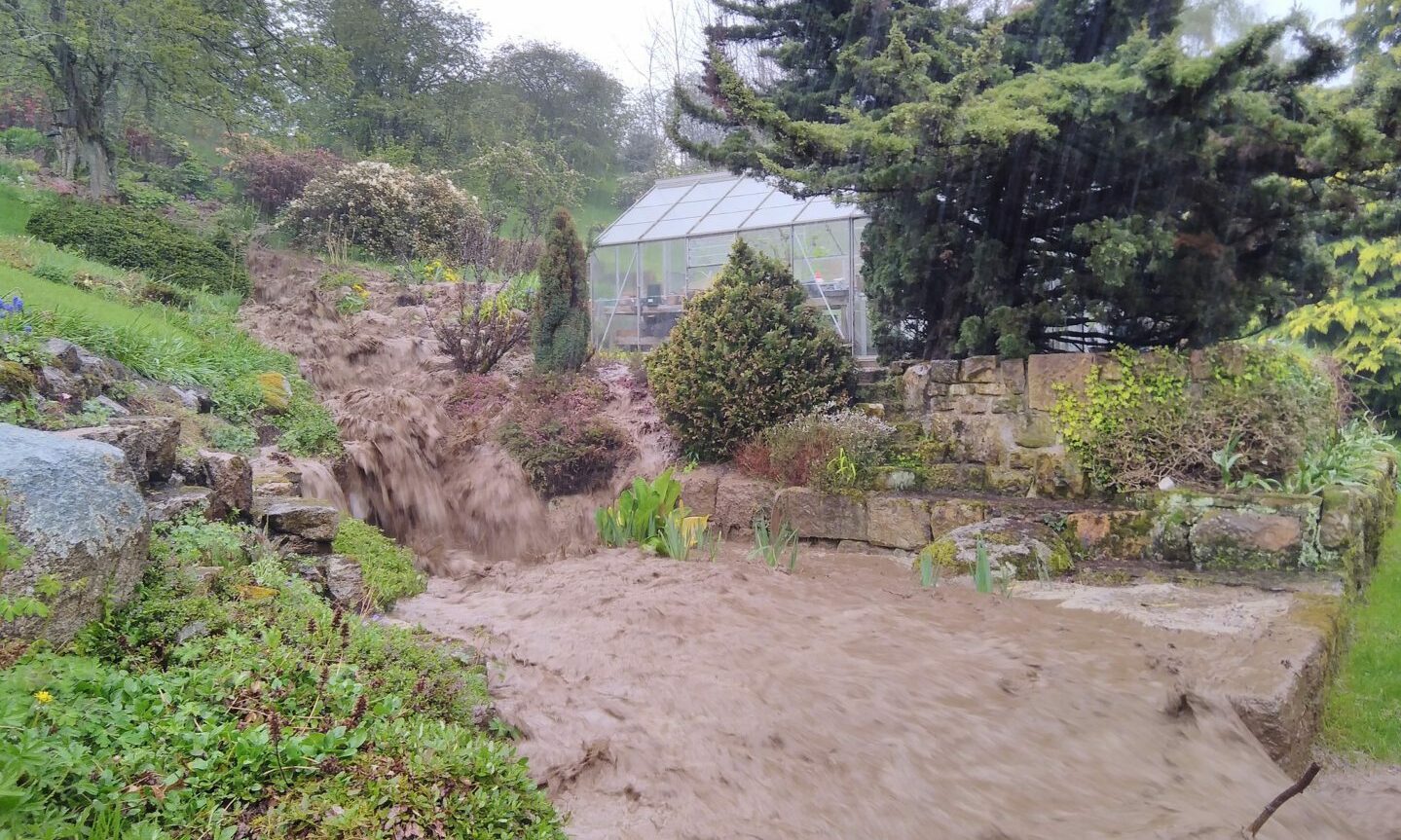 View at Alan Souter's garden showing torrent of muddy water pouring down hill towards camera.