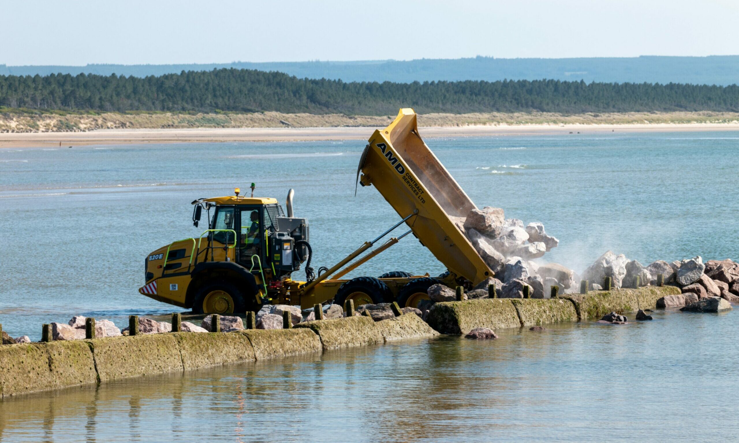Yellow dumper truck dropping rocks into the sea viewed from the side. 