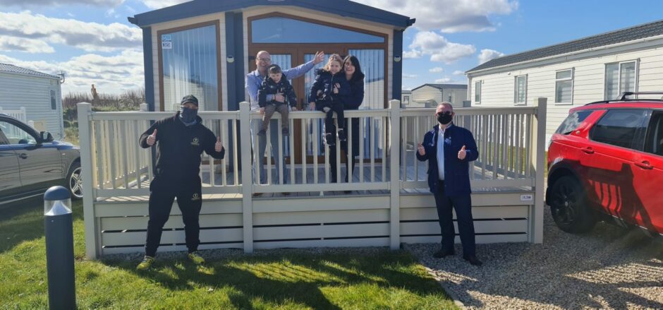 Scott Fraser poses in front of luxury log cabin he won in a Bounty Competitions live draw