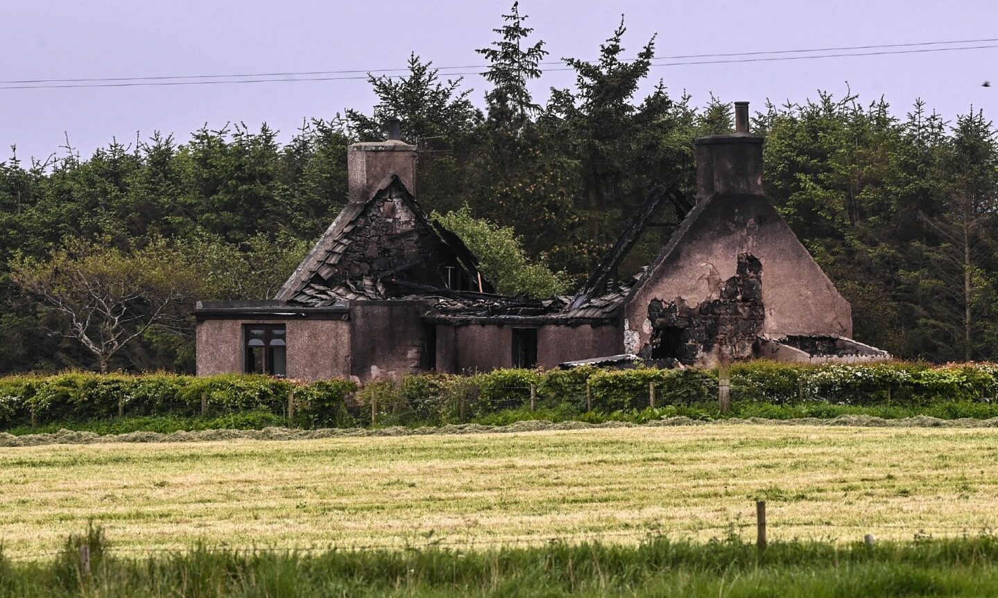 The ruined cottage in a rural setting with a field in the foreground. 