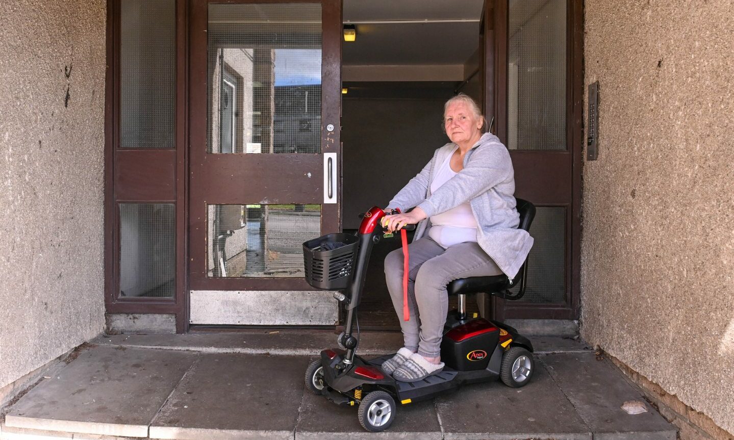 Heather Petrie in a mobility scooter outside the communal door to her building. 