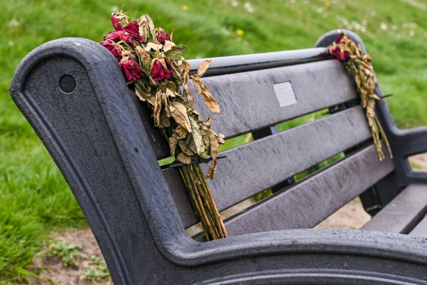 Withering flowers tied to a memorial bench at Aberdeen Beach