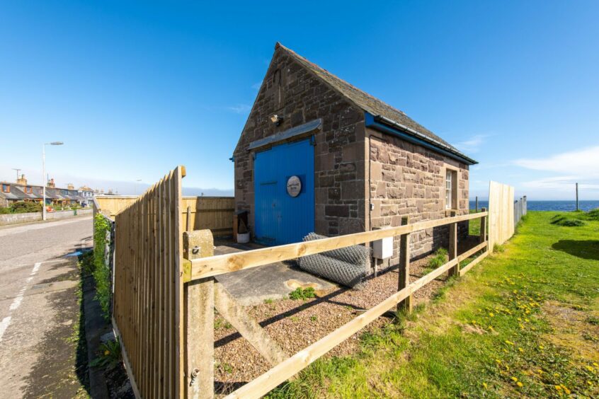 Side view of coastguard bothy in Cowie near Stonehaven with fence and blue coloured entrance. 