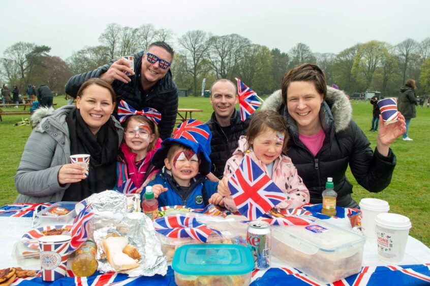 Parents and children amidst various Union Jack themed decorations and merchandise, including cups, flags, and hats, at Aberdeen's Big Lunch held in Duthie Park to commemorate the king's coronation.