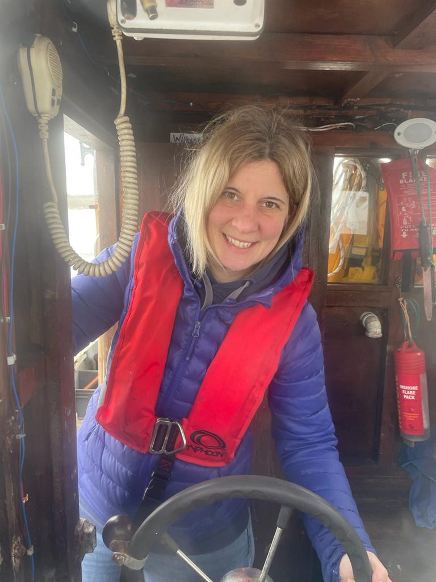 Beth Oxley wearing a lifejacket while holding the wheel of a boat. 