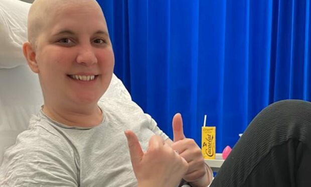 Beth Oxley sitting in a hospital bed with two thumbs up.