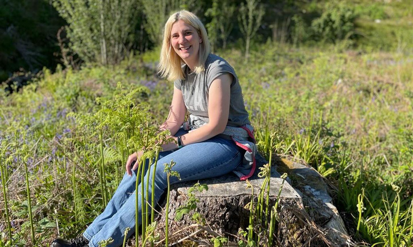 Beth Oxley sitting on a rock in a field. 