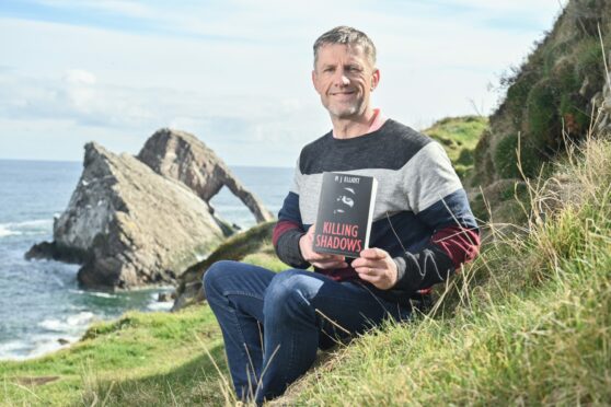 Crime writer Michael Elliott pictured with his latest book and the Bow Fiddle Rock in the background. Image: Jason Hedges/ DC Thomson