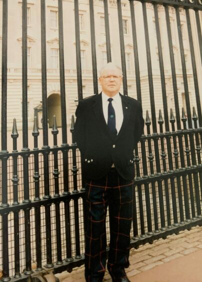 John Ramage MBE, pictured in tartan trews and smart jacket, by the high gates of Buckingham Palace after being made a member of the British Empire. 