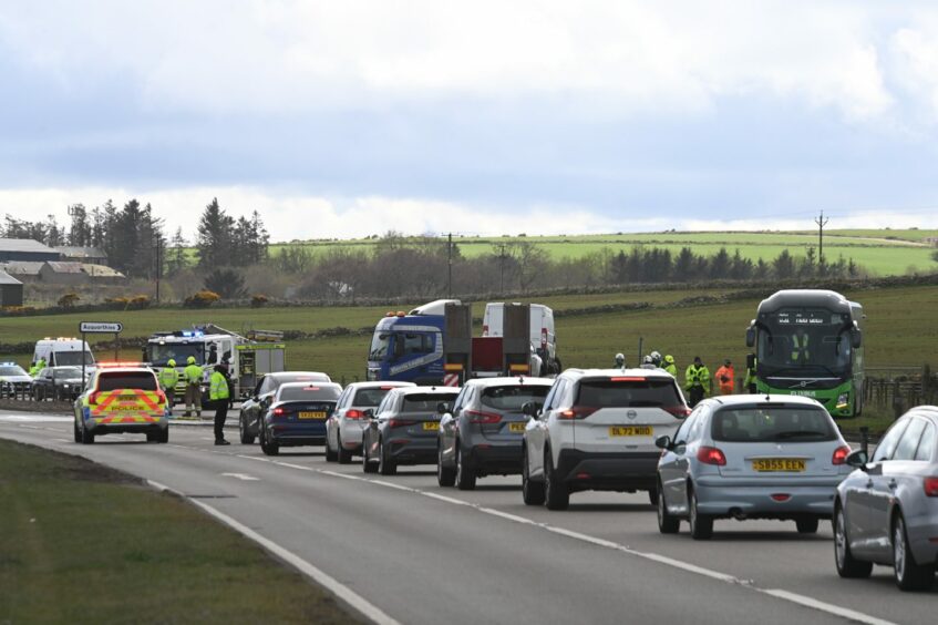 A queue of vehicles forms on the road with police directing traffic after the crash involving a green bus, pictured on the grass verge, and a lorry, seen blocking the A92. 