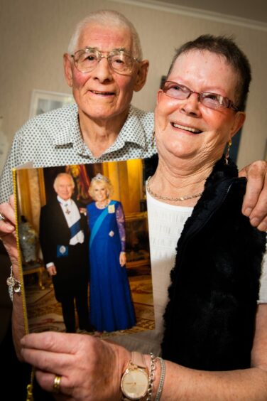 Willie and Helen Howie standing next to each other holding a card they received from King Charles and Queen Camilla.
