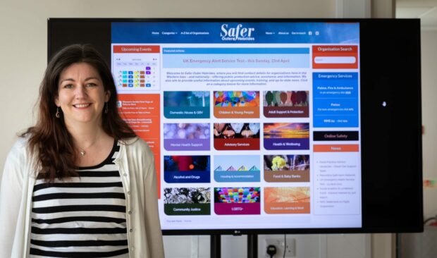 A woman stands in front of a display of webpage. The webpage says 'Safer Hebrides'.