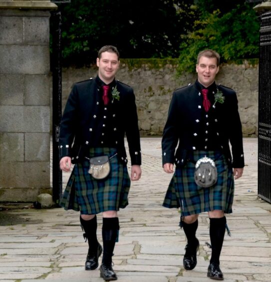 Ranald and his brother Ricky are pictured walking through a granite gateway, both wearing matching kilts, black waistcoats, red ties and a black jacket. 