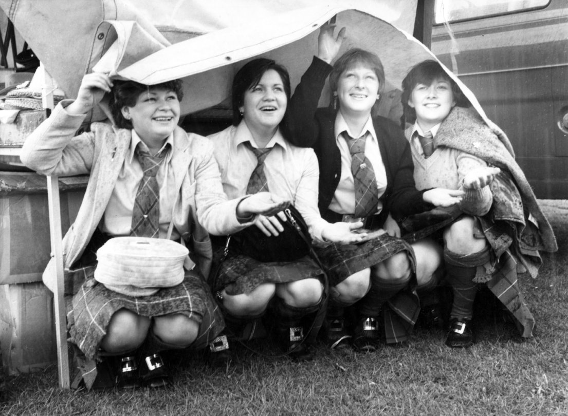 Members of Deeside Ladies Pipe Band under a tarp to shelter from the rain