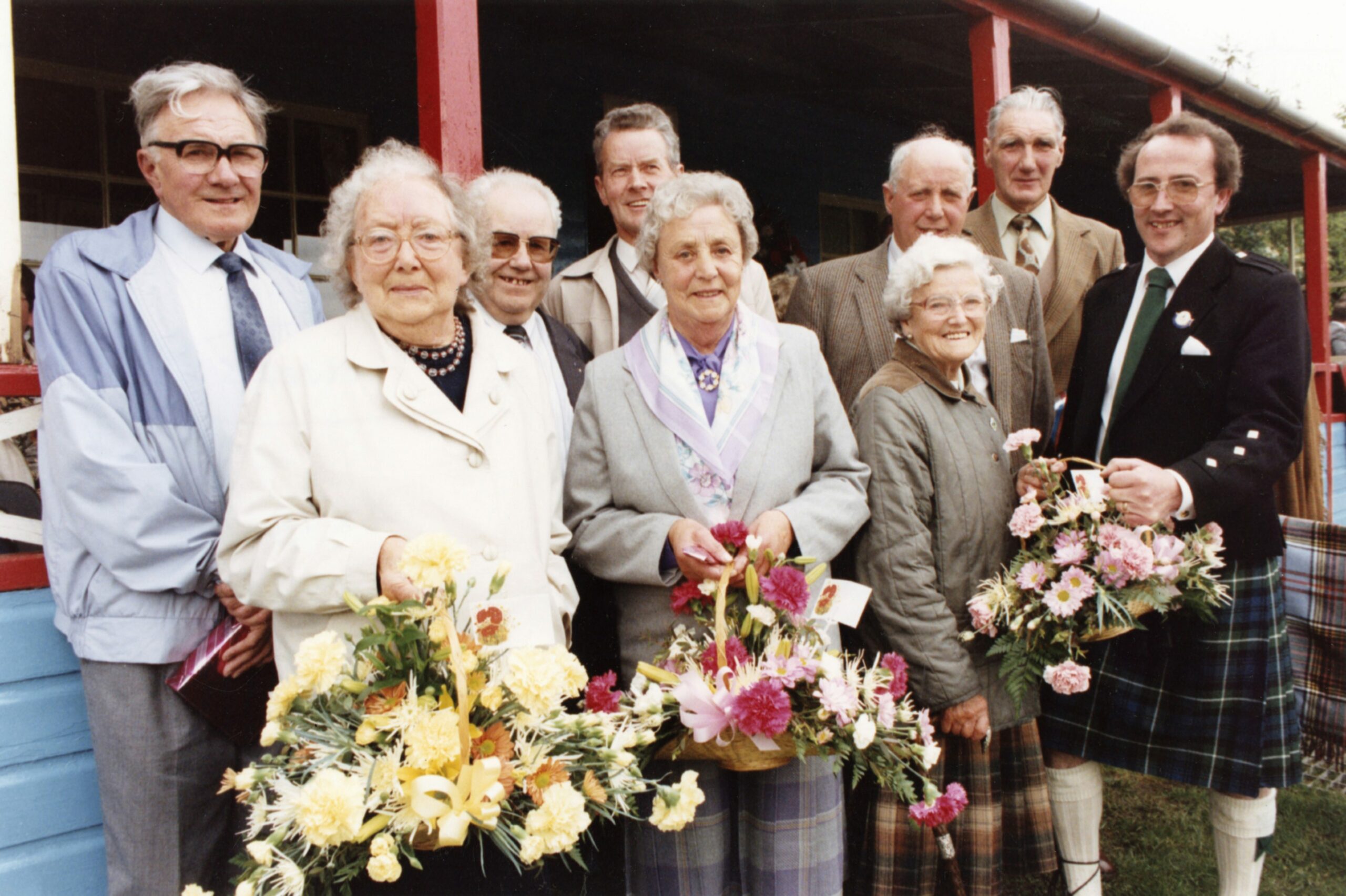 A group of older women and men volunteers holding flower baskets with Bob Forsyth