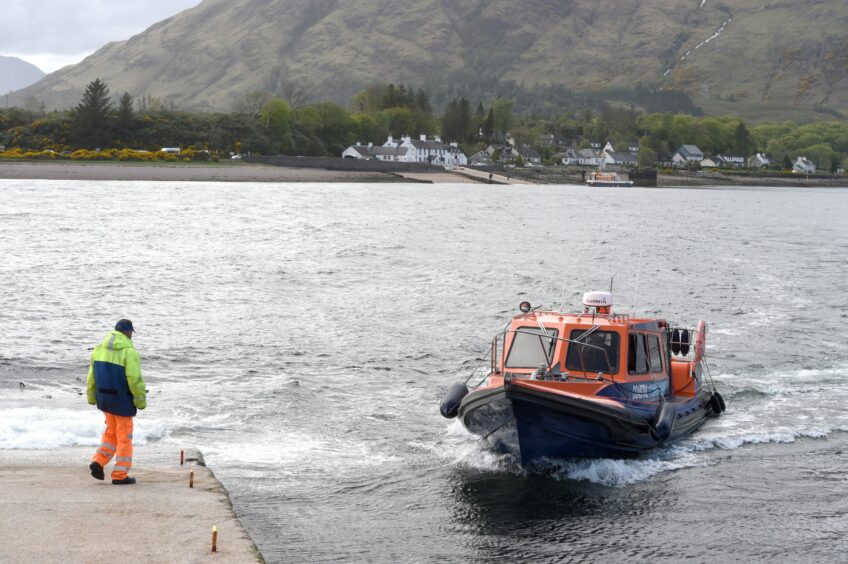 A Highland Council passenger ferry coming into dock at Corran Ferry with one man waiting on the pier-side to tie up the boat. 