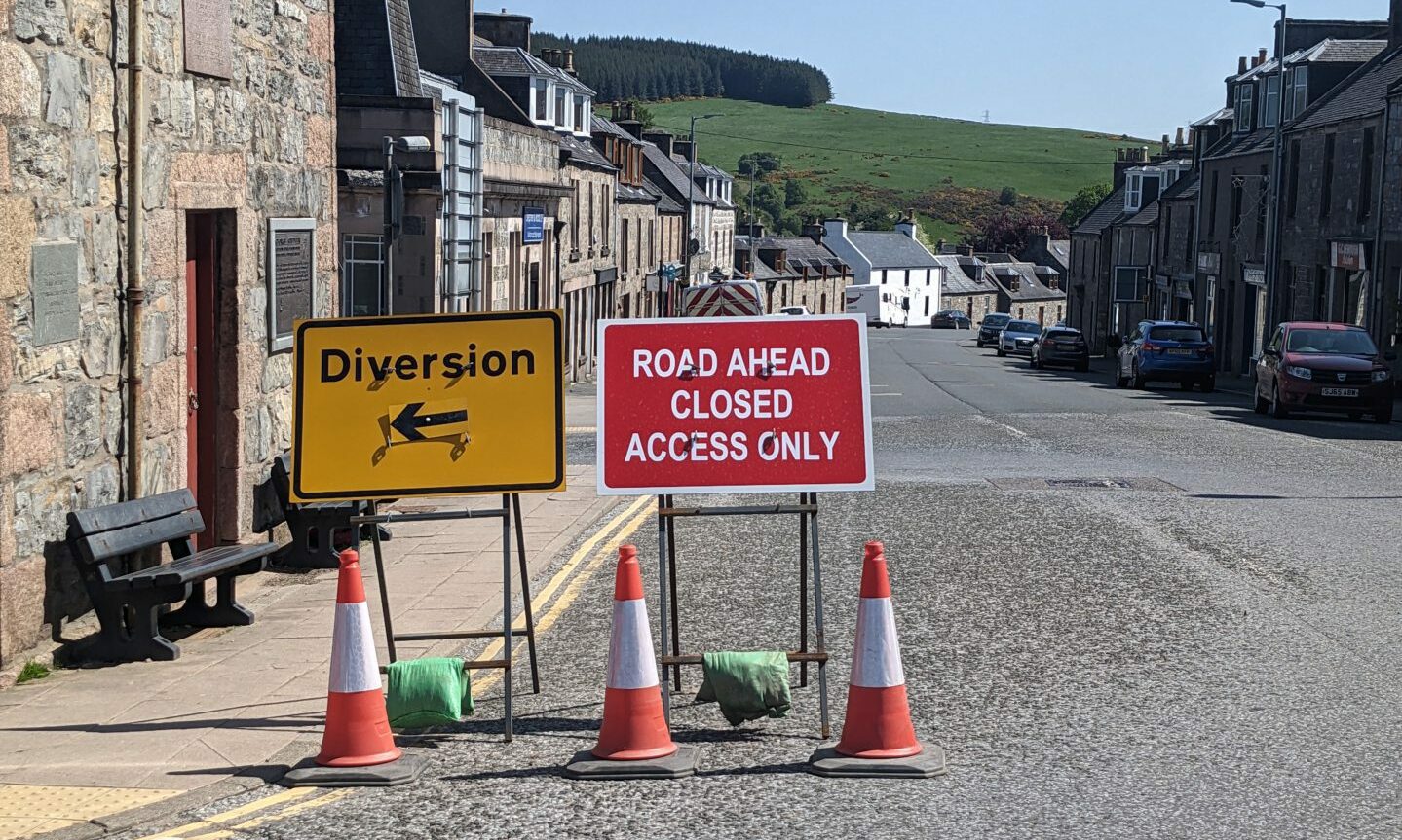 Two signs at The Square in Dufftown. One pointing left signalling the diversion, the other saying "road ahead closed access only". 