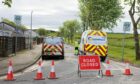 Scottish Water vans at the scene of the burst water pipe at Bucksburn on Newhills Avenue behind cones and a road closure sign.