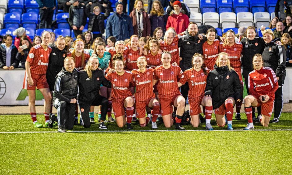Aberdeen Women players and coaches in two rows with arms around each other. The front row is knelt down on one knee