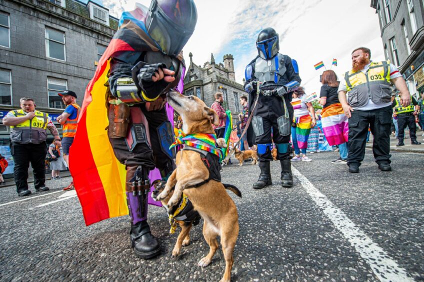 Two cosplayers with their terrier dog wearing a rainbow bandana 