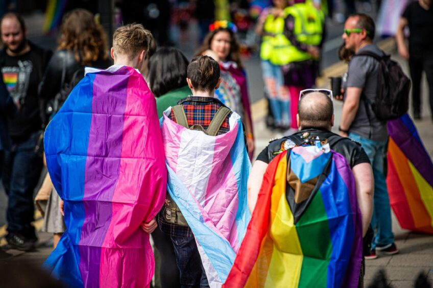Three people wearing different LGBTQ+ flags.