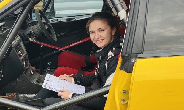 Co-driver Emily Easton-Page holding a notepad in the passenger seat of a yellow rally car.