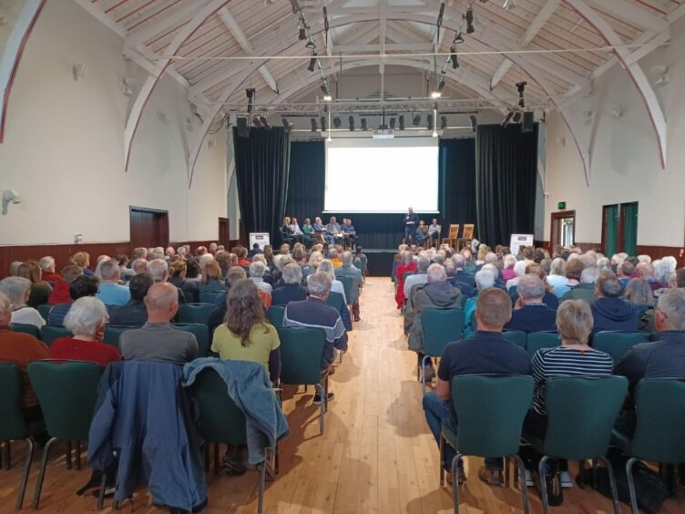 Scores of campaigners pack a village hall for a community meeting.