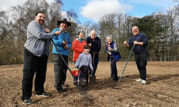A photo of a group of smiling volunteers including children holding rakes on the community garden patch in Culloden.