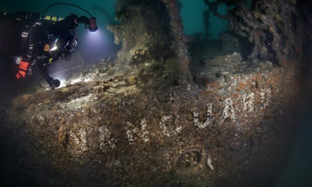 Stern of the Vanguard wreck with the name just about visible through rust. Diver shining a light on the name.
