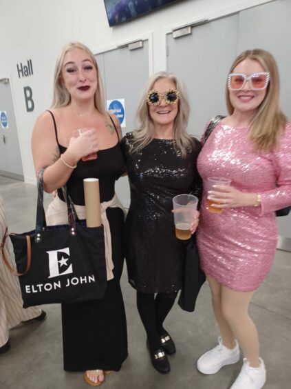 Kristen Hagentogler, Allison Adelmann and Emily Hagentogler holding plastic cups from P&J live, one of them has a bag of merch with Elton John's name printed on it