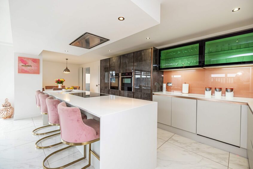 Pristine kitchen featuring white countertops, flooring and island along with pink velvet seats.