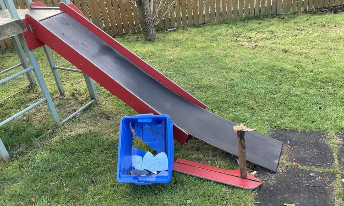 Side-on view of a red slide which has had plastic sides broken off it. 