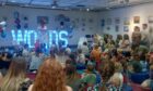 Miss Lossie Mouth in front of a sign saying "words" performing to packed room in Elgin Library.