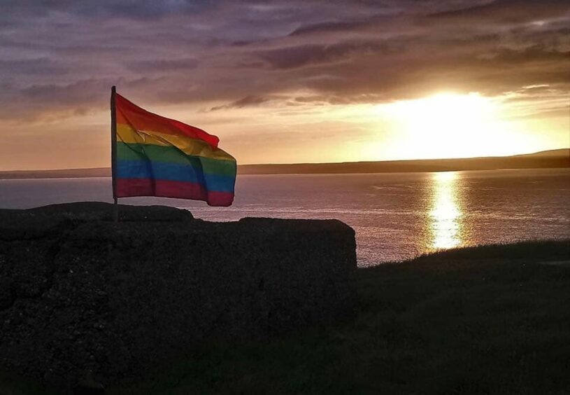 Rainbow LGBTQ+ flag with sunset in the background.