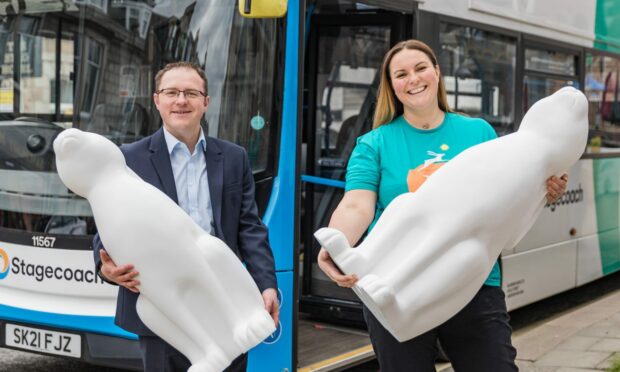 Two people stand with large hare sculptures next to a bus. The people are Daniel Laird and Fiona Fernie.